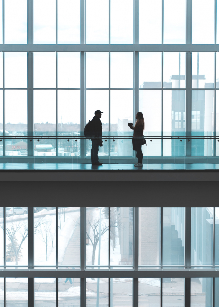 Two People Talking on Walkway inside Glass building